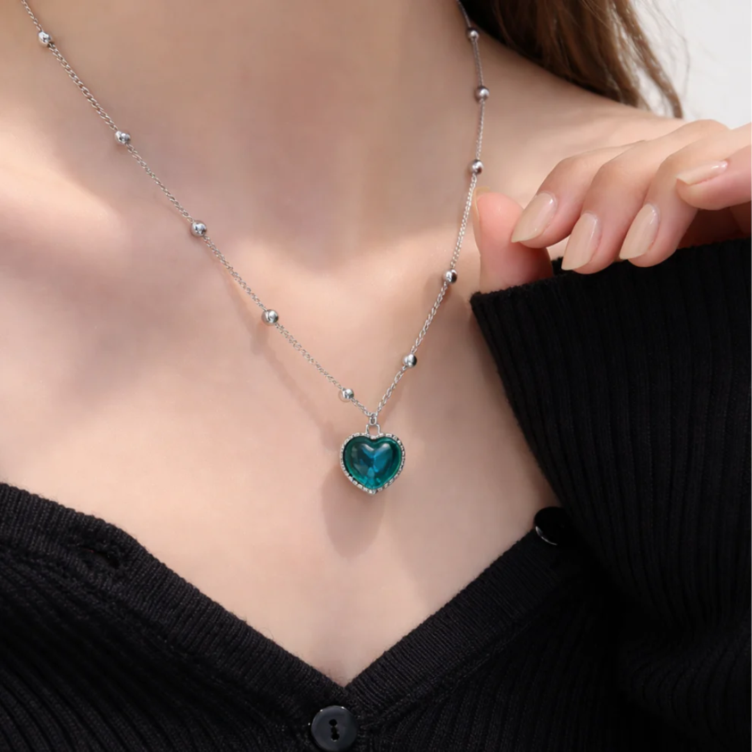 Close-up of the Aura Heart necklace worn with a black knit top, the heart pendant showing deep teal