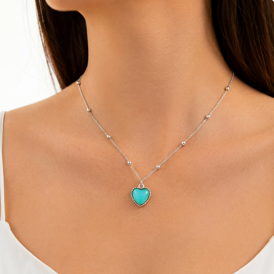 Woman in a white top wearing the Aura Heart necklace, the heart pendant showing turquoise on a fine silver-tone beaded chain